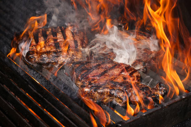 Western cowboy hatted chef of a large camp is outdoors in Mojave Desert California grilling Tri Tip on big BBQ grills under a clear blue sky 