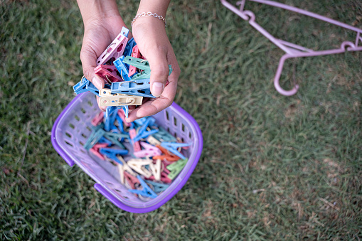A young Hispanic woman picking up a handful of clothespins from a basket to hang up in her garden. Close up. Concept of laundry tasks at home