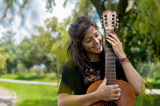 Portrait of beautiful Latin woman playing guitar relaxing outdoors in park.