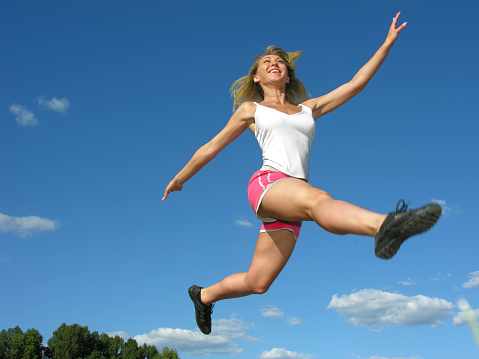 young athletic woman in a long jump on blue sky background, motion blur
