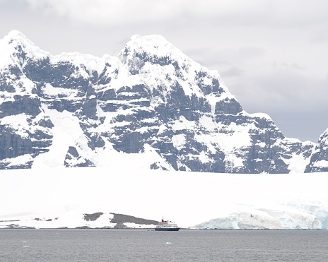 A small expedition cruise vessel for tourists, anchored by Palmer Station, Anvers Island, is dwarfed by the surrounding mountains of the Antarctic Peninsula