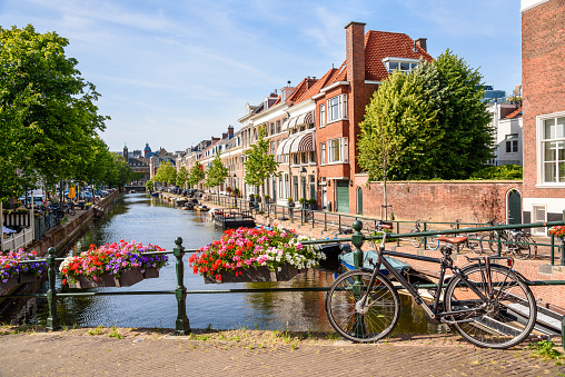 Canal lined with brick row houses on a sunny summer day. A bicycle chained to a bridge railing is in foreground. The Hague, Netherlands.