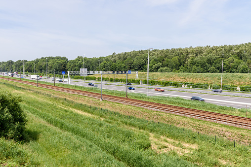 Motorway running parallel to railway tracks in the countryside of Netherlands on a summer day. Zoetermeer, Netherlands.