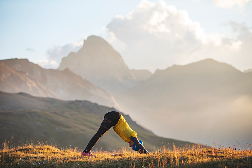 Young adult woman practicing yoga in mountains at sunset with beautyfull view
