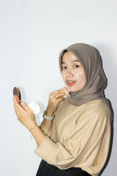 istock young hijab women applying make up on her face while holding a mirror. Isolated background 1477615371