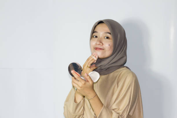 istock young hijab women applying make up on her face while holding a mirror. Isolated background 1477615387