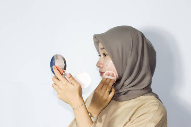 istock young hijab women applying make up on her face while holding a mirror. Isolated background 1477615535