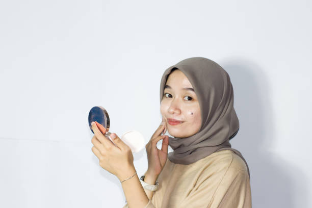 istock young hijab women applying make up on her face while holding a mirror. Isolated background 1477615613