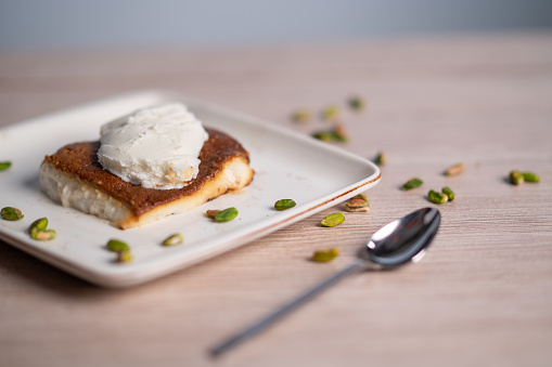 Turkish traditional dessert kazandibi with ice cream and pistachios on wooden background.