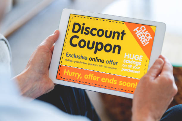 Man looking at an online discount coupon on a digital tablet. Man looking at an online discount coupon on a digital tablet. He is sitting on a sofa at home. Discount Codes stock pictures, royalty-free photos & images