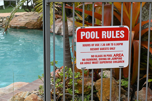 Red and white pool rules sign on a pool fence