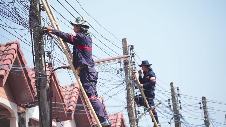 Asian male employees are climbing up a very high light pole using bamboo stairs.Power lines  or internet cable fibre optic are being connected on high poles. very dangerous.