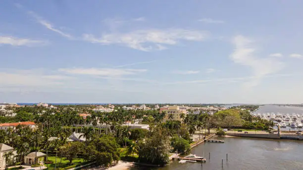 Aerial View of Beach-Front Housing Overlooking a Vibrant Beach Filled with Blue Ocean Waves, Rocks, Seaweed, Beach Umbrellas, Surf Boards, & People on the Sandy Shoreline in Palm Beach, Florida at Midday During Springbreak 2023