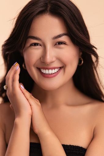 Merry Asian woman with long black hair clasping hands and looking at camera with smile during beauty routine