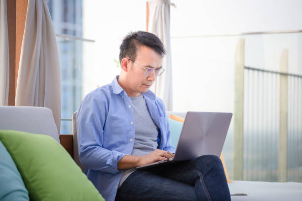 istock Asian man using laptop sitting on sofa at home, Man working from a laptop at the terrace 1477644870