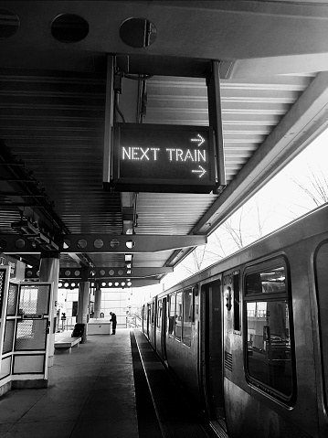 The final Midway stop on Chicago's Orange Line connecting to Midway Airport. In black and white, the 'next train' sign with train.