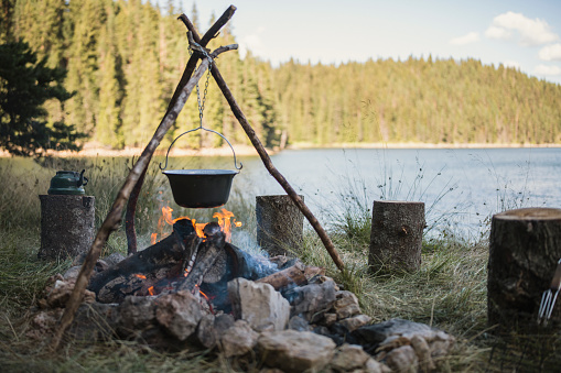 Shot of a camp in nature with pot with soup cooking over the campfire.
