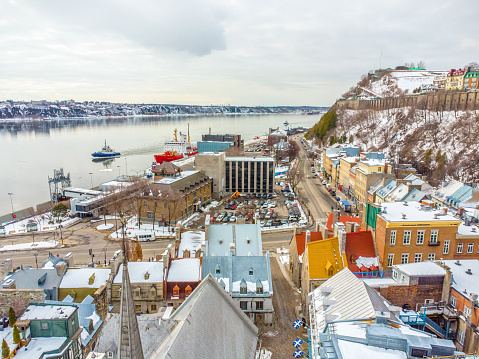 Aerial view of St. Lawrence river coastline downtown Quebec city with Champlain Boulevard, houses and a boat passing by during a winter day