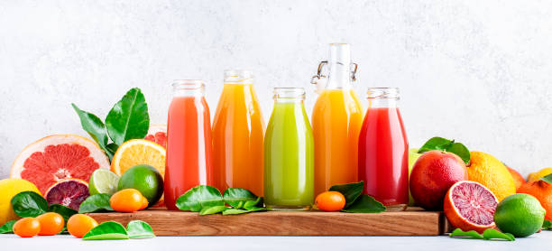 Summer beverages. Citrus fruit juices, fresh and smoothies, food background. Mix of different whole and cut fruits: orange, grapefruit, lime, tangerine with leaves and bottles with drinks, banner stock photo