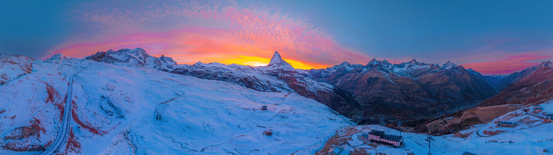 Aerial panorama view of Matterhorn mountain with amazing colorful twilight romantic sky in Switzerland. Wide establishing nature landscape sunrise or sunset of Zermatt travel ski resort in Swiss alps.