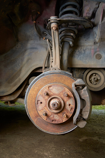old and rusty car disk brake and caliper with steering knuckle and suspension without wheel, car care and safety concept, car maintenance in selective focus with copy space