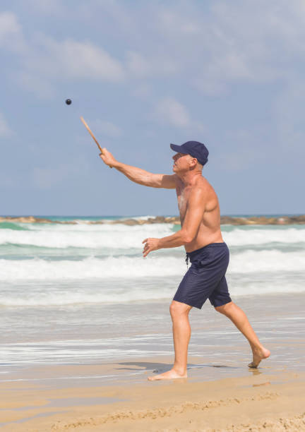 um homem maduro bonito bate uma bola enquanto joga matkot na praia - matkot - fotografias e filmes do acervo