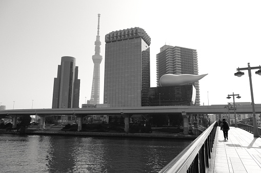Woman walking on the Azuma bridge, crossing the Sumida river in Tokyo. In the distance, Sumida ward skyline with the Tokyo Skytree, the tallest tower in the world, height 634 mt and the Asahi Breweries headquarters.