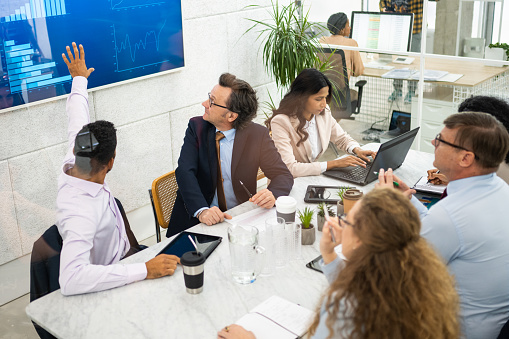 Businessman showing at TV screen and explaining chart to his coworkers in conference room.