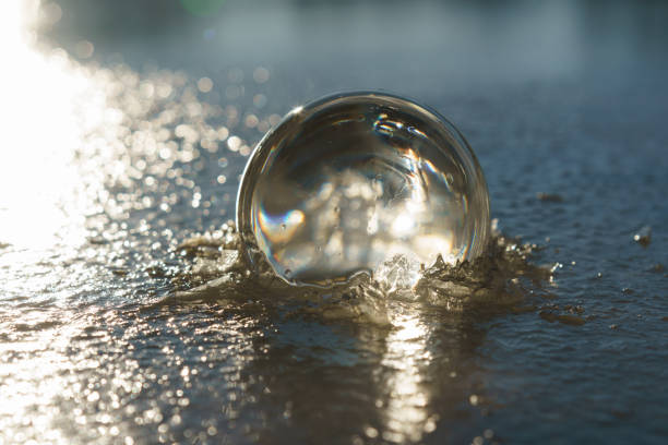 Photography of clear crystal ball lying on the water of the beach. Miracle view. Splashes of the water. Concept of the beauty in nature. Close up. Back lit