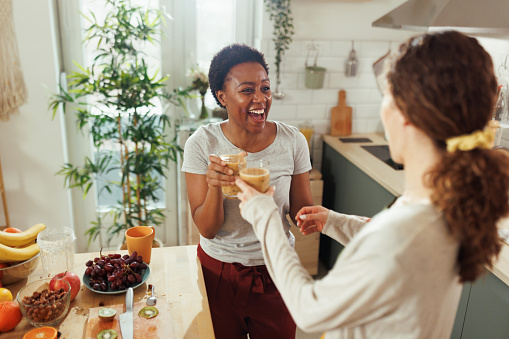 Female friends having celebratory toast with smoothies in a domestic kitchen