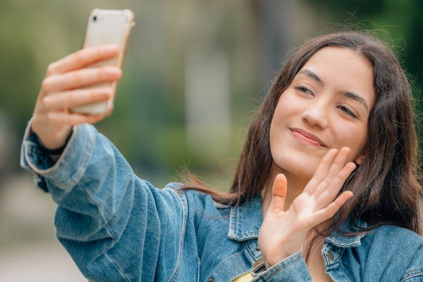 istock smiling girl waving with mobile phone online 1477704022