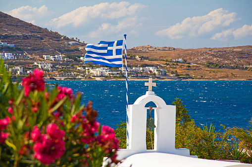 Greek seaside island Mykonos coast landscape with flag and religious church on a sunny day in the Aegean sea