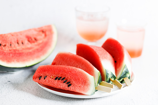 Watermelon slices with stick on white marble table. Summer vibes.