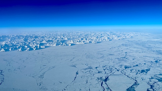 Long mountain range surrounded by vast ice sheet rising above sea; even bigger mountains in background