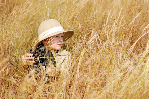 Young boy plays safari explorer with binoculars and bush hat in a field. happy adventure seeking kid playing outdoors.