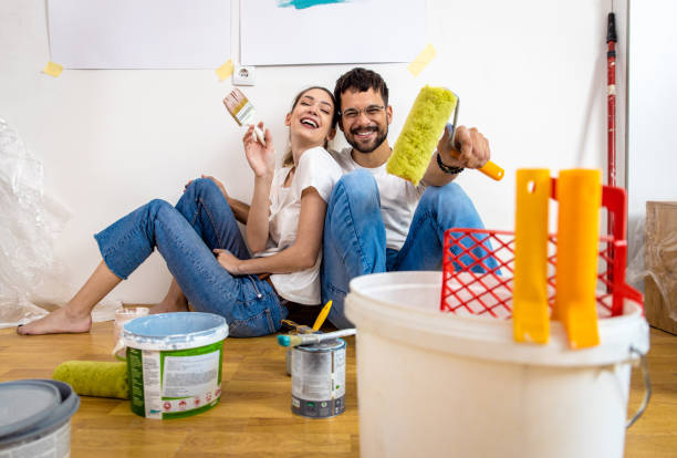 Young couple sitting on the floor choosing color for painting the wall in their home. stock photo