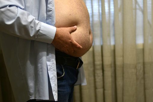 A man squeezes his big bare belly with his hands from below.