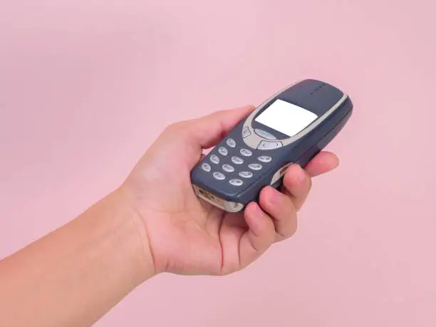 Close up hand holding mobile phone Nokia 3310 isolated on pink background. Female hand holding old used phone Nokia 3310.