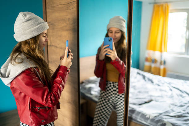 A young woman with a cell phone in front of a large mirror