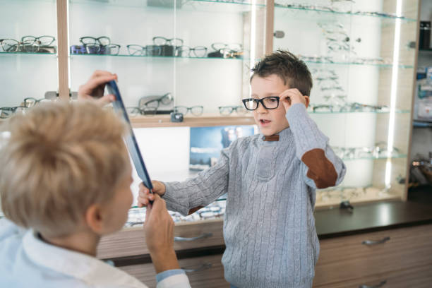 Young boy trying on different frames, while the Ophthalmologist helpfully holds up a mirror