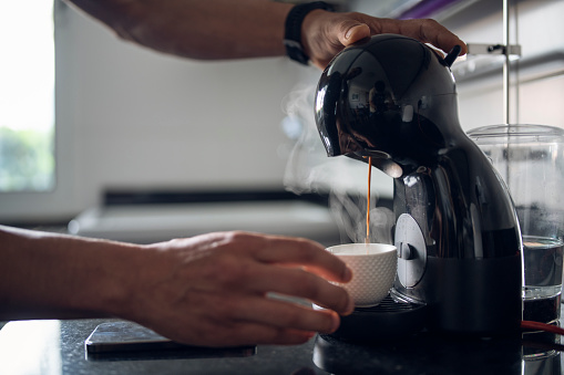 Close-up of unrecognizable man making coffee on coffee maker at home.