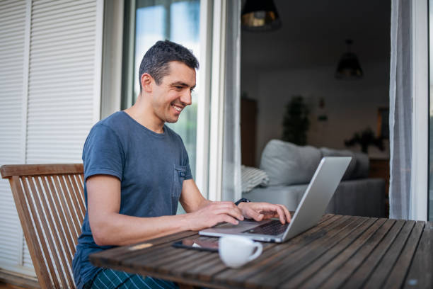 istock Smiling man on the balcony working on laptop. 1477723824