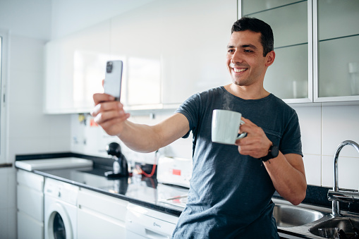 Man drinking coffee and taking a selfie/having a video call in the morning.