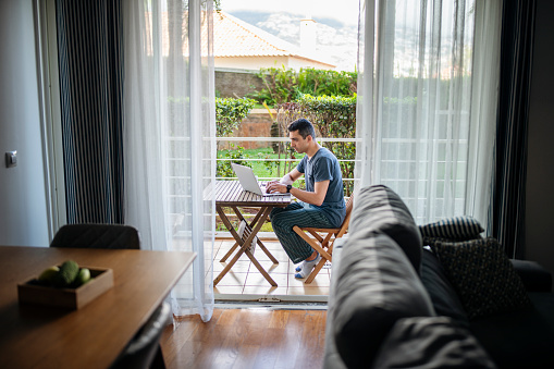 Man working from home on laptop and relaxing on balcony.