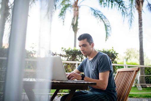 Mid adult businessman with laptop in home office, working outdoors on balcony.