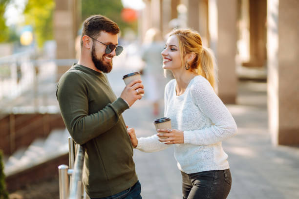 istock Young couple having fun talking, drinking coffee while walking in the morning city. 1477724354