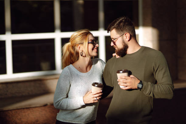 Young couple having fun talking, drinking coffee and using the phone while walking in the morning city. Relaxation, youth, love, lifestyle, selfie, blogging.