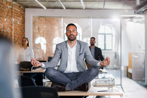 Businessman and his colleagues doing Yoga meditation exercises on tables in the office.