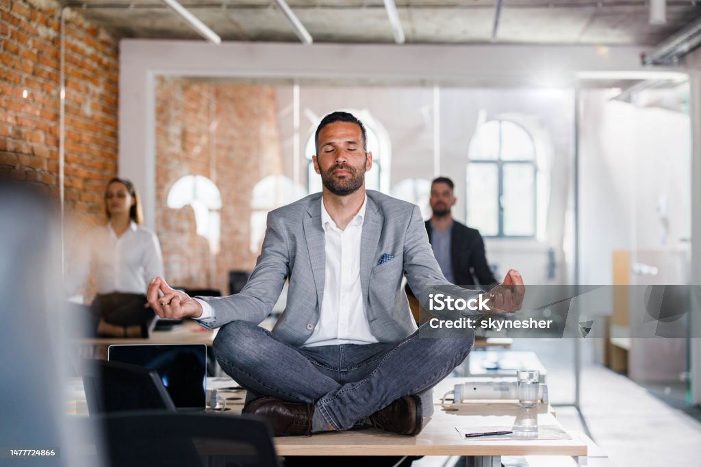 Maintaining mental balance in the office! Businessman and his colleagues doing Yoga meditation exercises on tables in the office. Office Stock Photo
