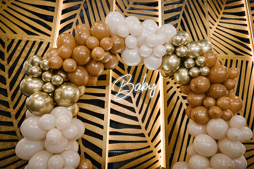 Text baby. Arch decorated with brown, beige and golden balloons. Celebration baptism concept. Reception at birthday party on photo wall. Photo zone and location for celebration in the restaurant.